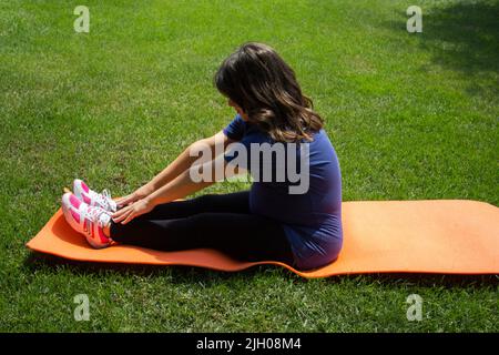 Immagine di una donna incinta seduta in un parco durante esercizi di aerobica. Preparazione al parto Foto Stock