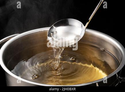 Dashi, brodo di zuppa, e le basi della cucina giapponese. Sfondo nero. Vapore. Sessola con mestolo. Foto Stock