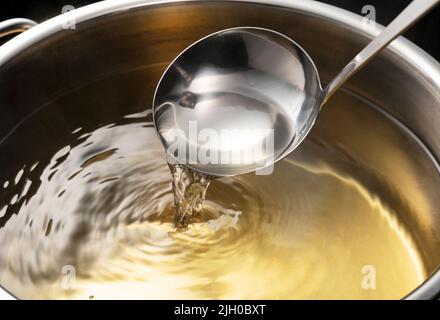 Dashi, brodo di zuppa, e le basi della cucina giapponese. Sfondo nero. Vapore. Sessola con mestolo. Foto Stock