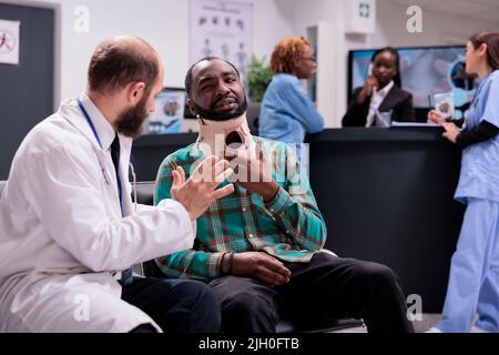 Persona infortunata con colletto al collo che parla con il medico su appuntamento medico nella lobby della sala d'attesa. Uomo in dolore con rinforzo di schiuma cervicale cercando di curare lesioni da incidente, ricevendo il trattamento. Foto Stock