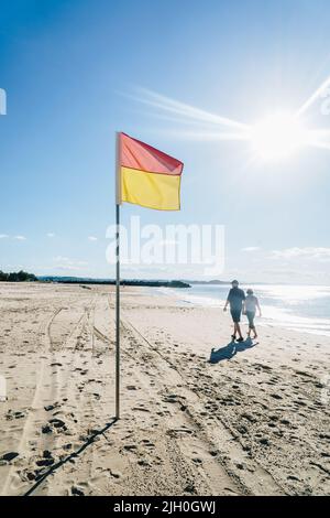 Coppia a piedi vicino alla bandiera del bagnino sulla Gold Coast Foto Stock