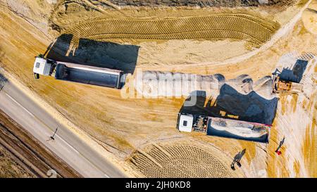 Sopra la vista dall'alto, sopra due dumper ribaltabili come il sollevamento del rimorchio per scaricare il carico, frazione, piccola pietra frantumata che il cingolato bulldozer è spinta dentro Foto Stock