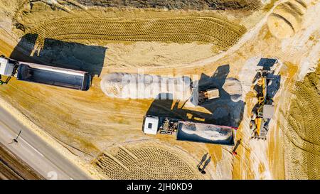 Sopra la vista dall'alto, sopra due dumper ribaltabili come il sollevamento del rimorchio per scaricare il carico, frazione, piccola pietra frantumata che il cingolato bulldozer è spinta dentro Foto Stock