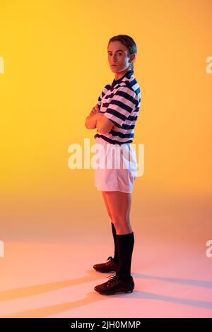 Ritratto di donna caucasica rugby giocatore con le braccia incrociate su neon giallo illuminazione Foto Stock