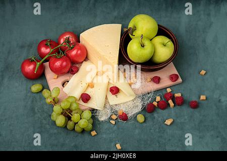 pezzo di formaggio con mele e pomodori su un asse di legno su un bel sfondo Foto Stock