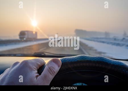 vista della mano del conducente sul volante della vettura durante la guida su una strada innevata scivolosa Foto Stock