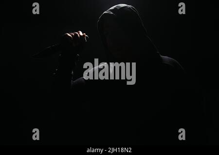 Silhouette di bandit in coltello con cappuccio isolato su nero Foto Stock