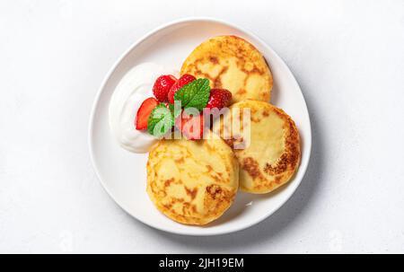 Pancake al formaggio casolare con panna acida e bacche su sfondo grigio. Foto Stock