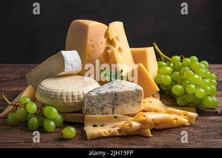 Formaggi di diverse varietà e uve su sfondo ligneo. Foto Stock