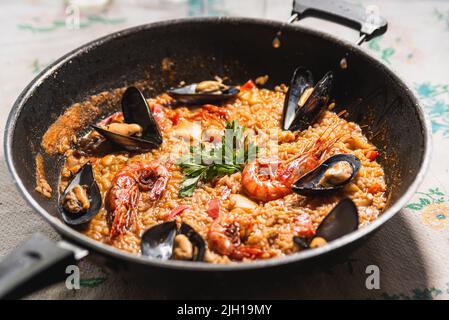 Paella tradizionale spagnola di pesce o arroz caldoso all'interno di una padella nera con gamberetti, cozze, vongole e prezzemolo. Paella tradizionale fatta in casa all'interno della paella Foto Stock