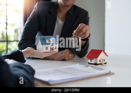 Gli agenti immobiliari accettano di acquistare una casa e dare le chiavi ai clienti presso gli uffici della loro agenzia. Accordo concettuale Foto Stock