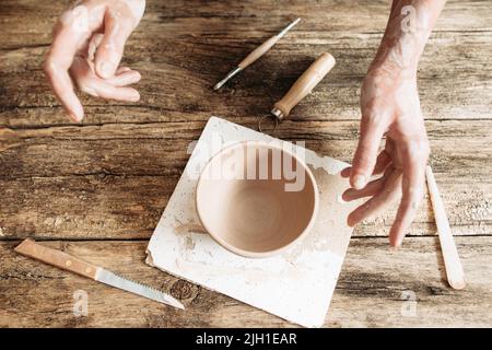 Mani che vanno a prendere ciotola di argilla dalla vista del tavolo di legno, concetto di terapia d'arte Foto Stock