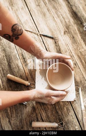 Le mani di Potter mettono la ciotola di creta sul tavolo di legno, primo piano Foto Stock