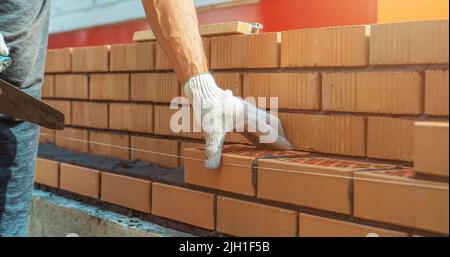 Il lavoratore o le mani del muratore che posano i mattoni vicino in su. Il muratore lavora a fila di mattoni. Muratura in cantiere. Foto Stock
