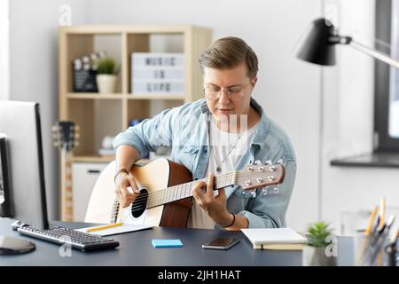 giovane che suona la chitarra seduto al tavolo di casa Foto Stock