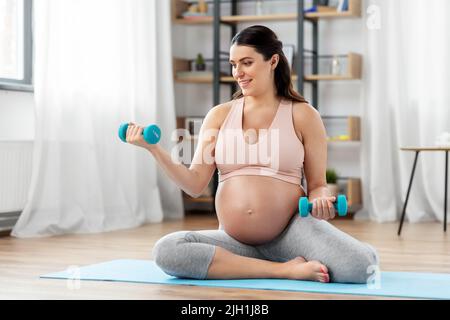donna incinta con manubri che fanno sport a casa Foto Stock