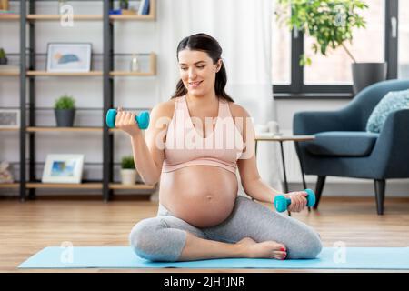donna incinta con manubri che fanno sport a casa Foto Stock