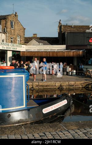 Skipton, North Yorkshire, Regno Unito. Persone socializzanti al Boathouse Bar con barche sul canale Leeds - Liverpool ormeggiate a Skipton. Foto Stock