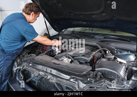 Elettricista che prova auto con multimetro in garage Foto Stock