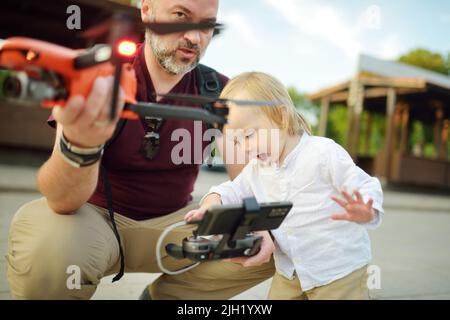 Padre e figlio guardano e navigano in un drone. Carino bambino ragazzo aiutando suo padre ad azionare un drone da telecomando. Tempo libero per tutta la famiglia. Foto Stock