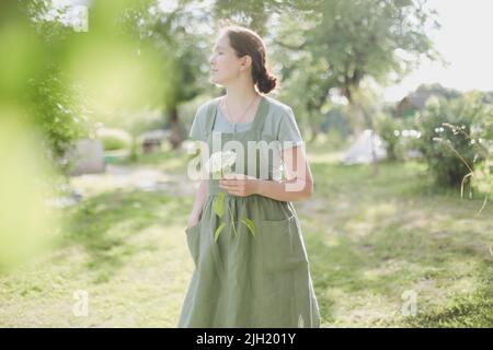 concetto di giardinaggio e professione - giovane donna in grembiule che tiene fiori in giardino in estate Foto Stock