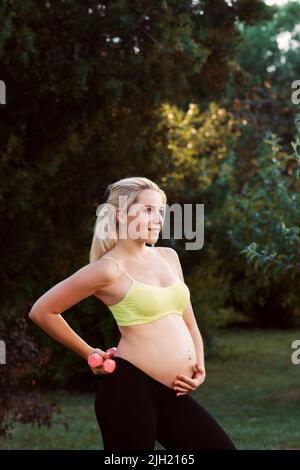 Donna incinta sorridente in posa con manubri Foto Stock