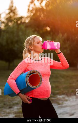 Donna incinta che beve acqua dopo il fitness Foto Stock