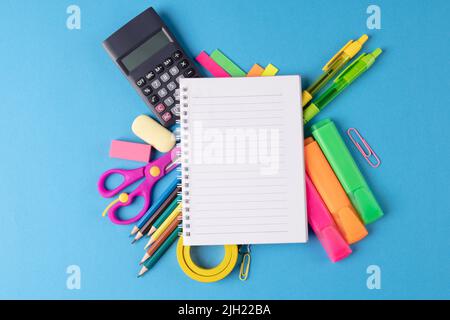 Immagine di vari materiali di consumo per ufficio, penne e notebook su sfondo blu Foto Stock