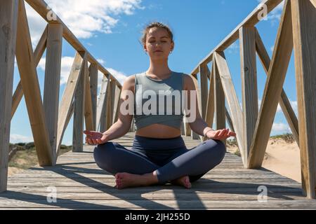 foto di una giovane donna che medita sulla passerella sotto il sole Foto Stock