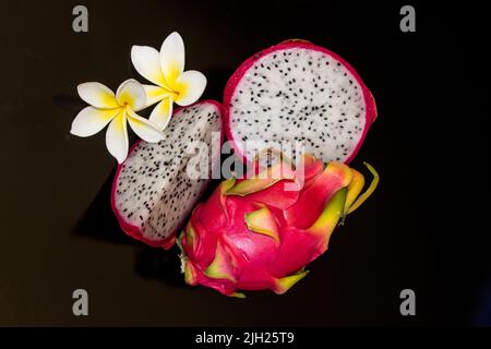 La natura morta del frutto del drago, su sfondo nero, insieme ai fiori di Frangipani Foto Stock