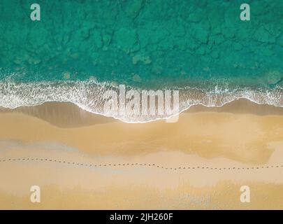 Orme umane su una spiaggia sabbiosa lungo il mare con onde che infrangono. Vista aerea direttamente sopra Foto Stock