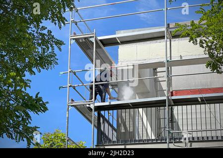 Ristrutturare un isolamento termico su un edificio residenziale il lavoratore rimuove il vecchio intonaco su una facciata di casa, pareti esterne, ponteggi, facciata, rivestimenti esterni, isolamento. Ristrutturazione, protezione termica completa, cantiere, costruzione residenziale, edificio residenziale, condominio, costruzione di appartamenti, industria delle costruzioni, operai delle costruzioni, boom delle costruzioni, industria edile. Foto Stock