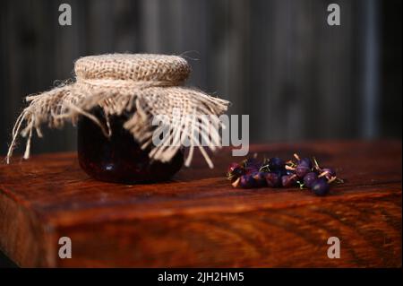 Ancora vita di un vaso di marmellata fatta in casa di uva spina e frutti di bosco freschi maturi su una superficie rustica di legno. Concetto di inscatolamento Foto Stock