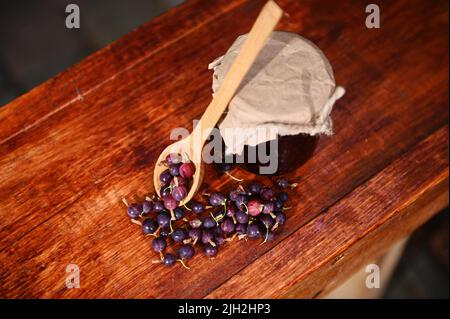 Vista dall'alto di un vaso di una marmellata fatta in casa, cucchiaio di legno e frutti di bosco su una superficie rustica di legno. Tradizioni culinarie Foto Stock