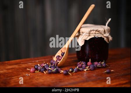 Vita morta. Vasetto di marmellata di frutti di bosco fatta in casa, cucchiaio di legno e frutti di bosco su una superficie rustica di legno. Concetto di inscatolamento Foto Stock