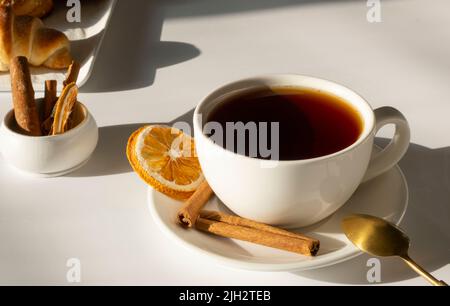 tè nella tazza bianca o in una tazza su sfondo bianco e chiaro con dolci freschi e croissant, colazione o concetto di mattina Foto Stock