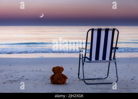 Sedia vuota e un giocattolo orsacchiotto sulla spiaggia Foto Stock