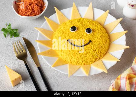 Insalata a forma di sole, con pollo, uova, carote e formaggio su sfondo grigio chiaro. Un'idea culinaria per le feste dei bambini Foto Stock