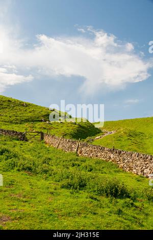 Derbyshire, Regno Unito – 5 aprile 2018: Cielo blu e verde erba verde verdeggiante, ma da un muro di pietra secco nel Parco Nazionale del Peak District Foto Stock