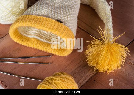 ancora vita di un elfo giallo cappello uncinato con materiali per la progettazione e la lavorazione di indumenti, posto su un fondo di legno. rotoli di lana Foto Stock