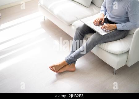 Riscaldamento a pavimento. Persona a piedi nudi che usa il computer in camera Foto Stock