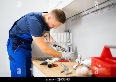 Felice Giovane Maschio Plumber che fissa il rubinetto in cucina Foto Stock