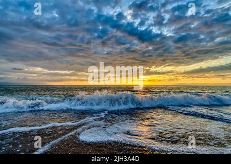 Un'onda dell'oceano sta rompendo contro Un cielo colorato del tramonto Foto Stock