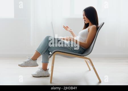 Confuso sconvolto abbronzato bella giovane donna asiatica scioccata da problemi di funzionamento con il portatile a casa soggiorno interno. Telecomando per comunicazioni a distanza Foto Stock