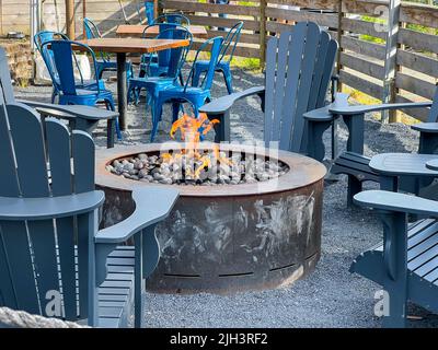 Vista ravvicinata delle sedie adirondack che circondano una fossa di fuoco piena di pietre all'interno di un patio all'aperto in un ristorante Foto Stock