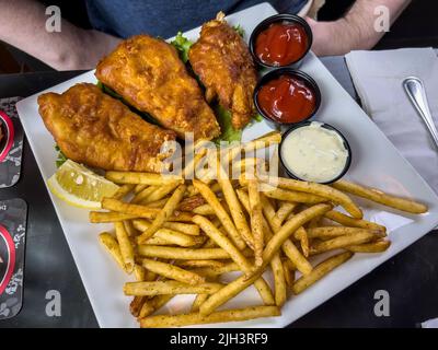 Vista ravvicinata di pesce croccante e patatine su un tavolo in un ristorante di fronte a un uomo caucasico Foto Stock