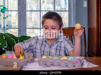 Il ragazzo sorridente esamina le uova colorate che ha appena creato per le celebrazioni di Pasqua e la caccia alle uova Foto Stock