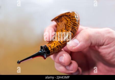 La mano dell'uomo tiene un tubo del corno del briar, lucidato splendidamente e tiene il suo tabacco fumante favorito Foto Stock