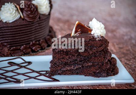 deliziosa fetta di torta al cioccolato fondente con panna montata e un triangolo di cioccolato Foto Stock
