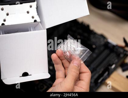 Il tecnico tiene in mano i piedini di montaggio per installare il radiatore o la scheda madre Foto Stock